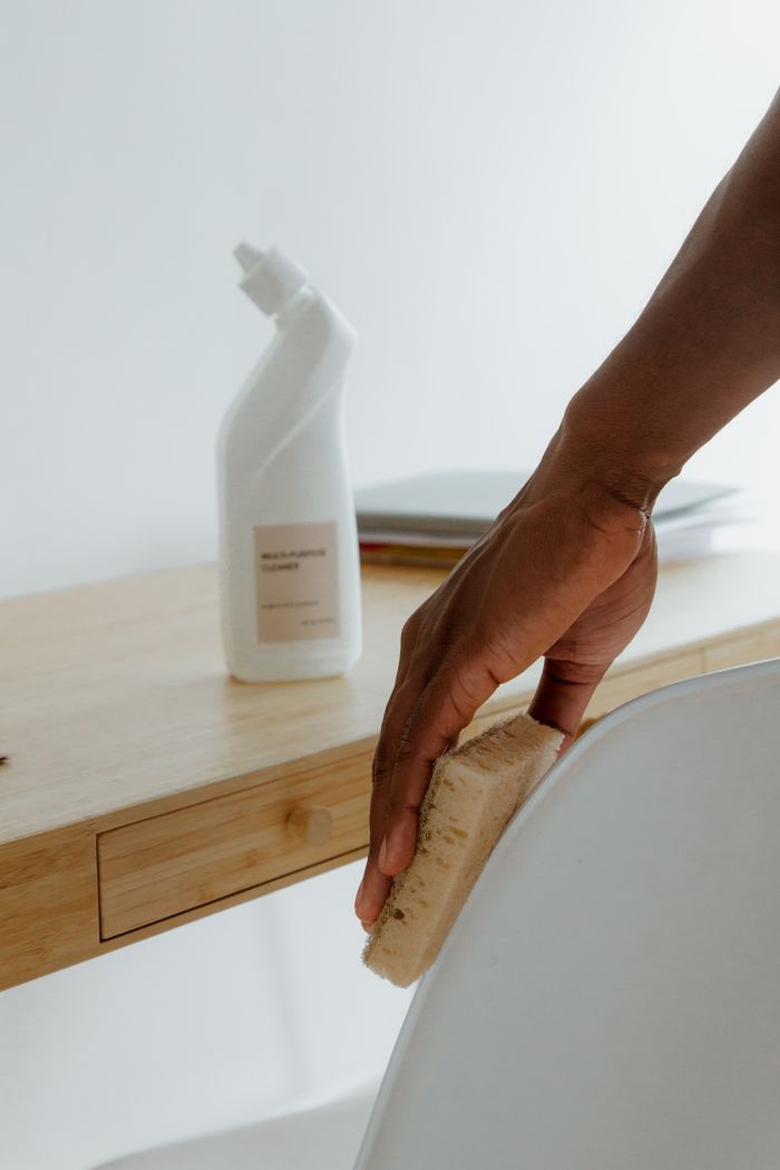 Chambre minimaliste avec une personne nettoyant une chaise à l’aide d’une éponge et d’un produit d’entretien.